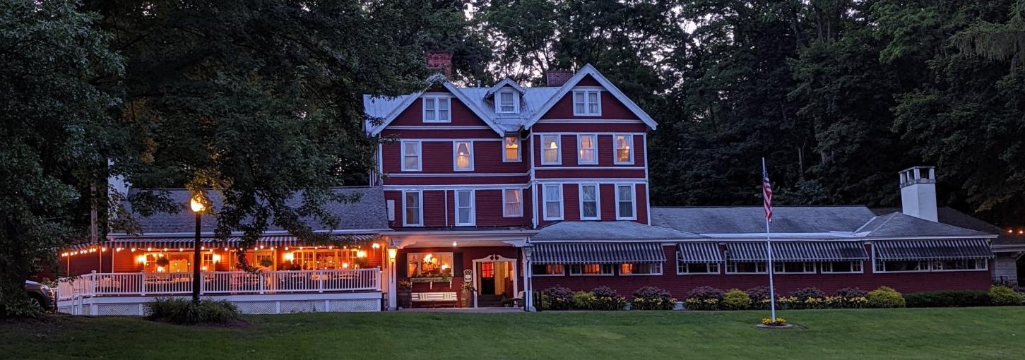 The red and white façade of a historic inn has a porch lied with lights.